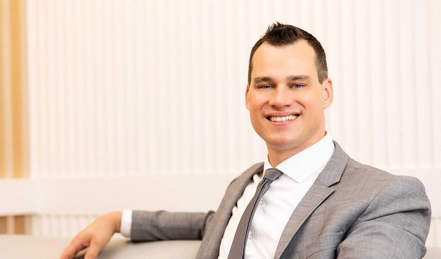 Dr. Brace smiling and sitting on couch with suit and tie