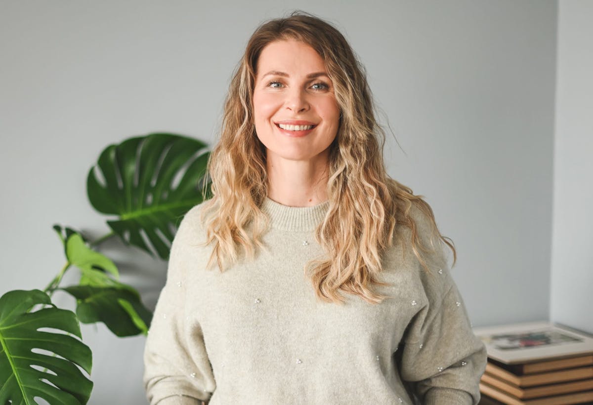 woman smiling and standing in front of plant and books