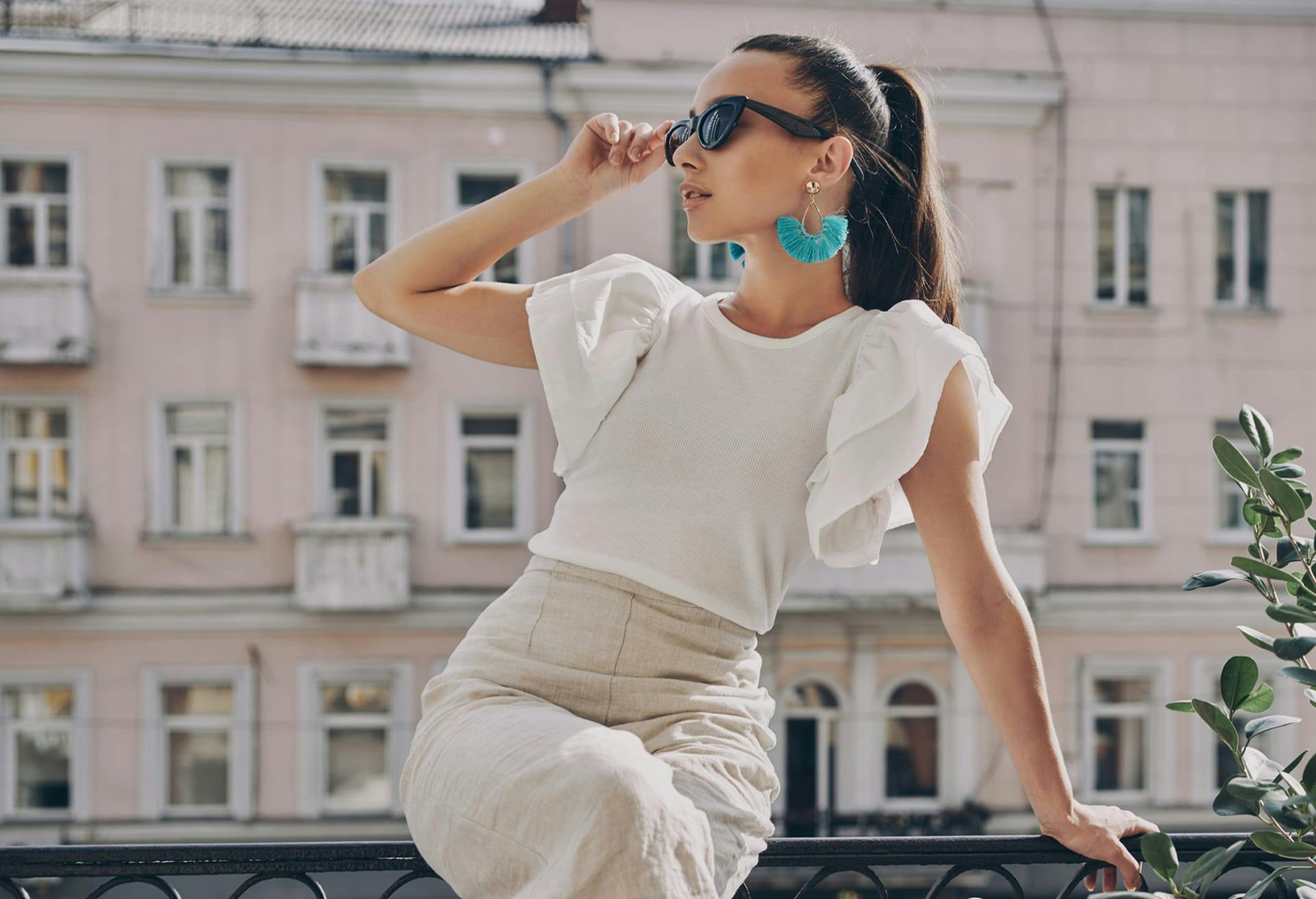 woman sitting on railing holding sunglasses to her face
