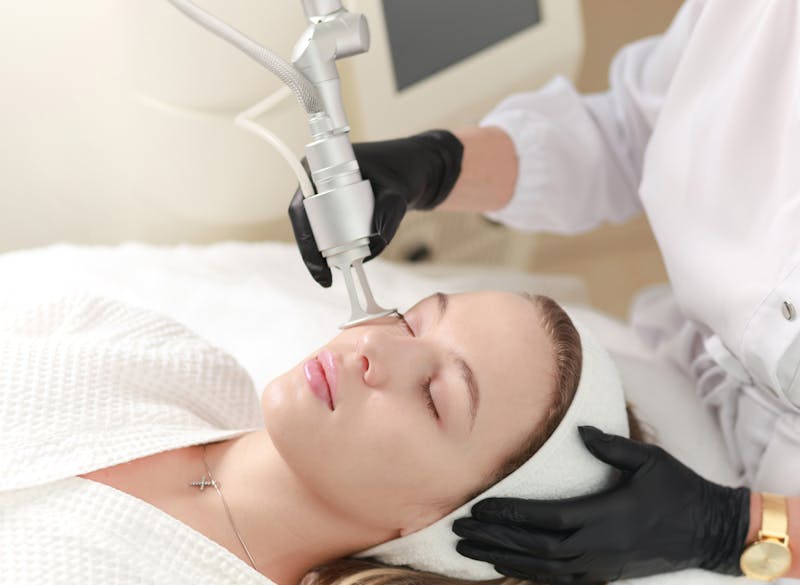 woman eyes closed on patient table with practioner applying a procedure