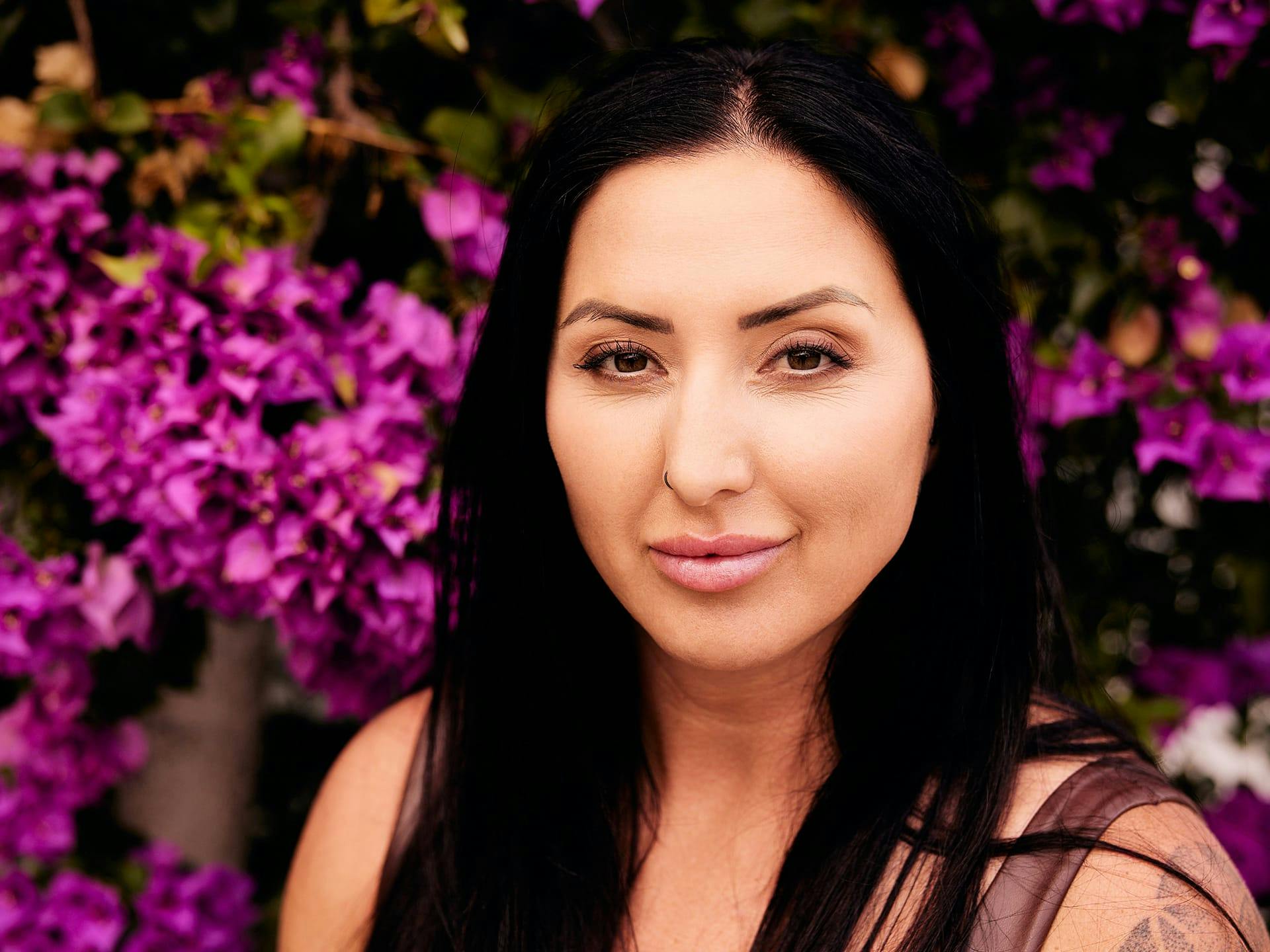 Woman with black hair standing in front of pink flowers