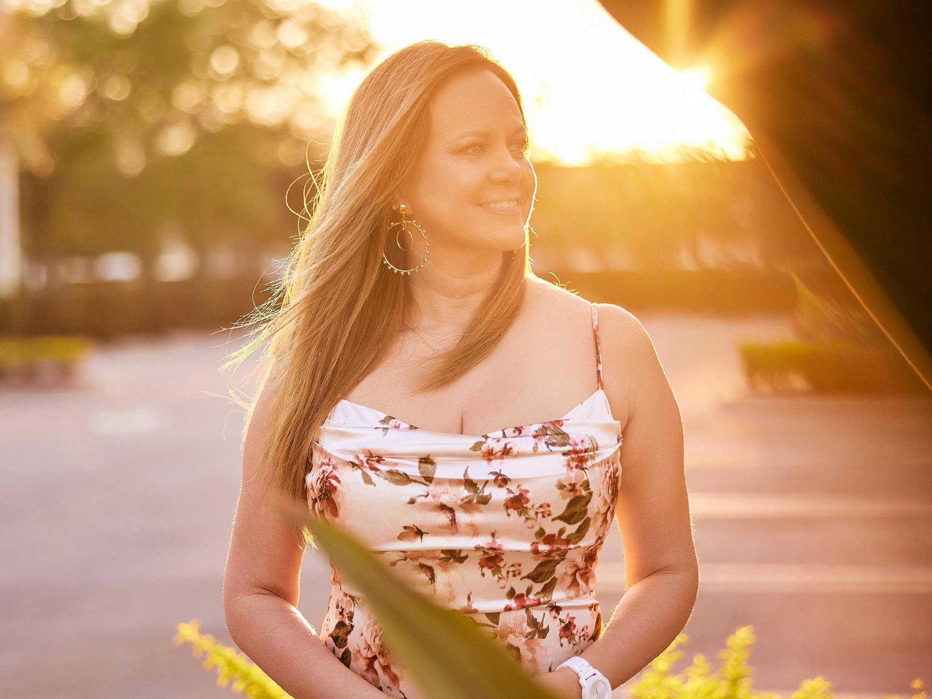 woman in white floral dress smiling with sunset behind her