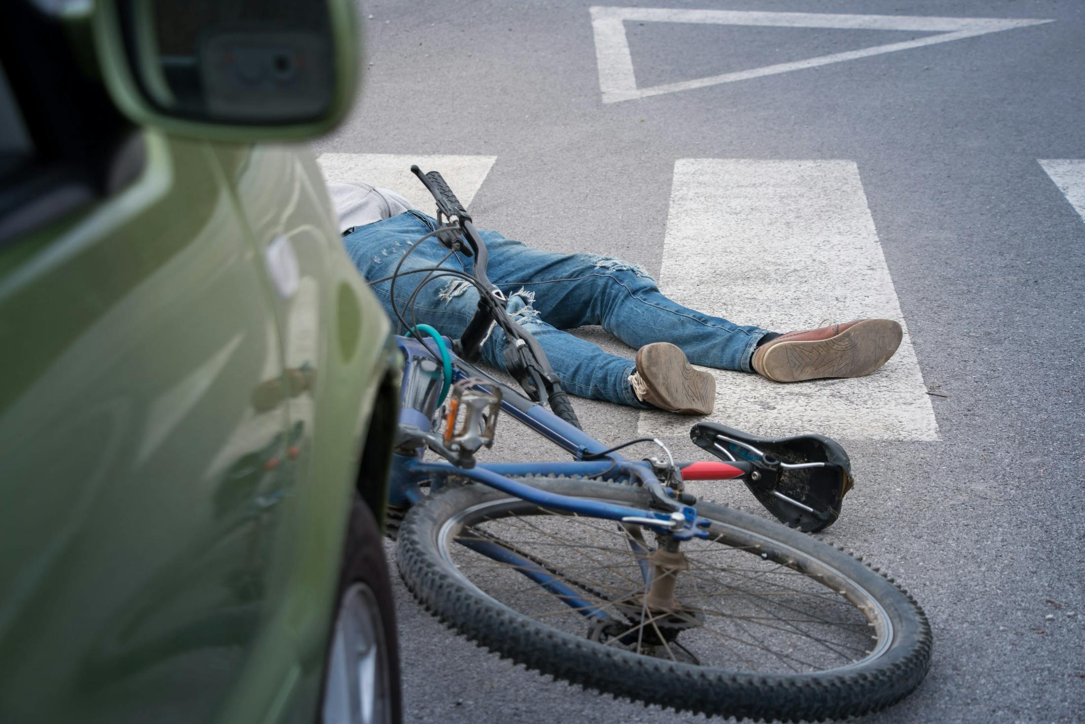 man lying in road next to bike and car