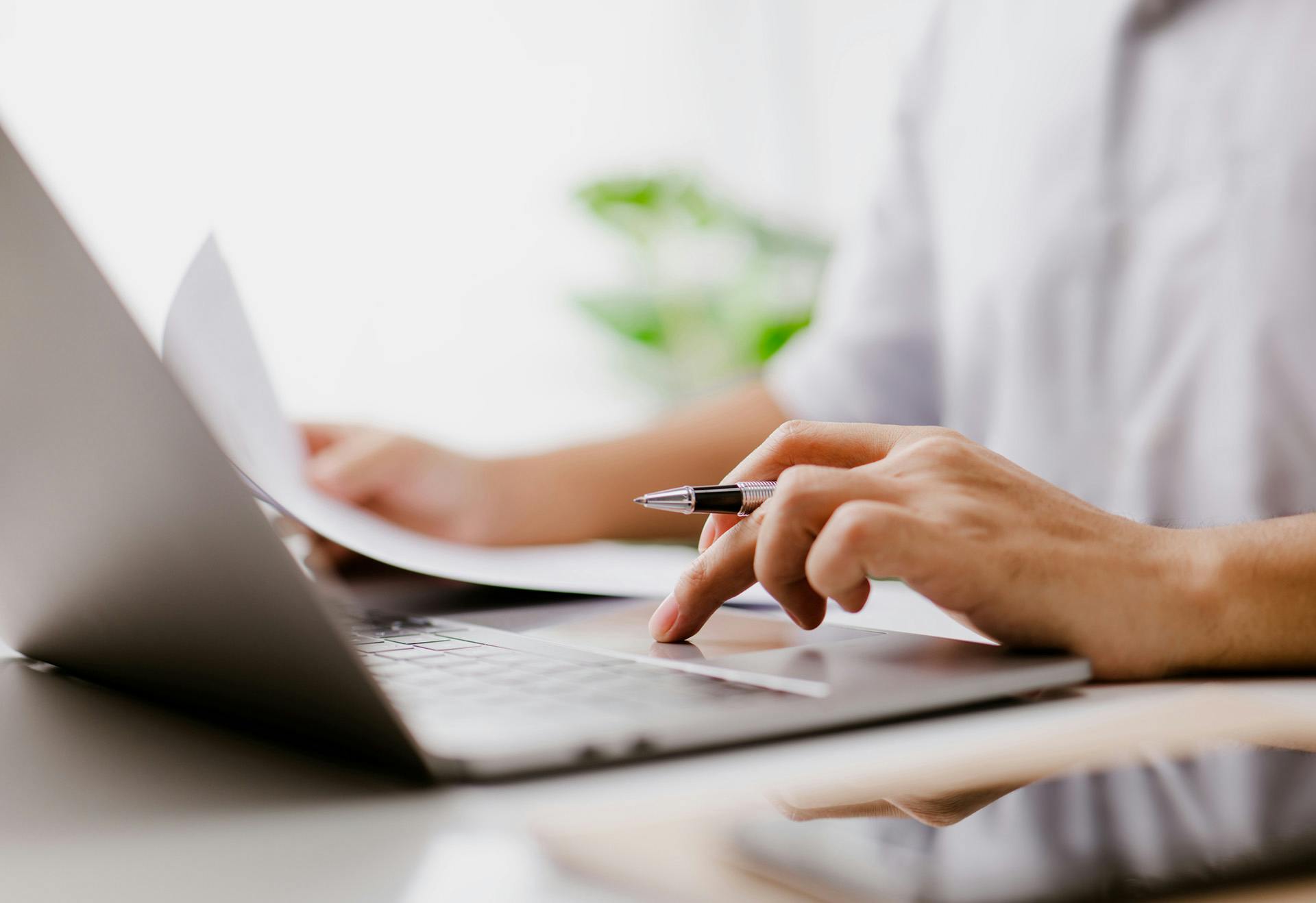 Person working on a computer holding papers.