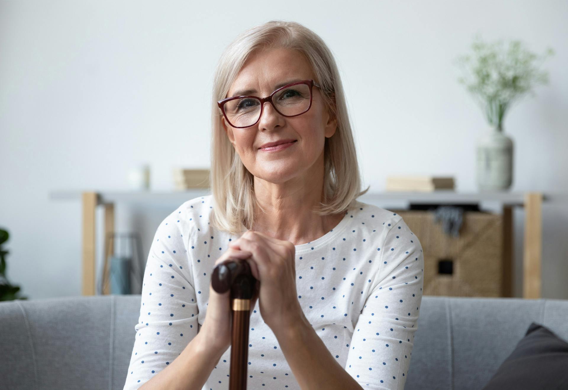 Elderly woman sitting on the couch holding a cane.