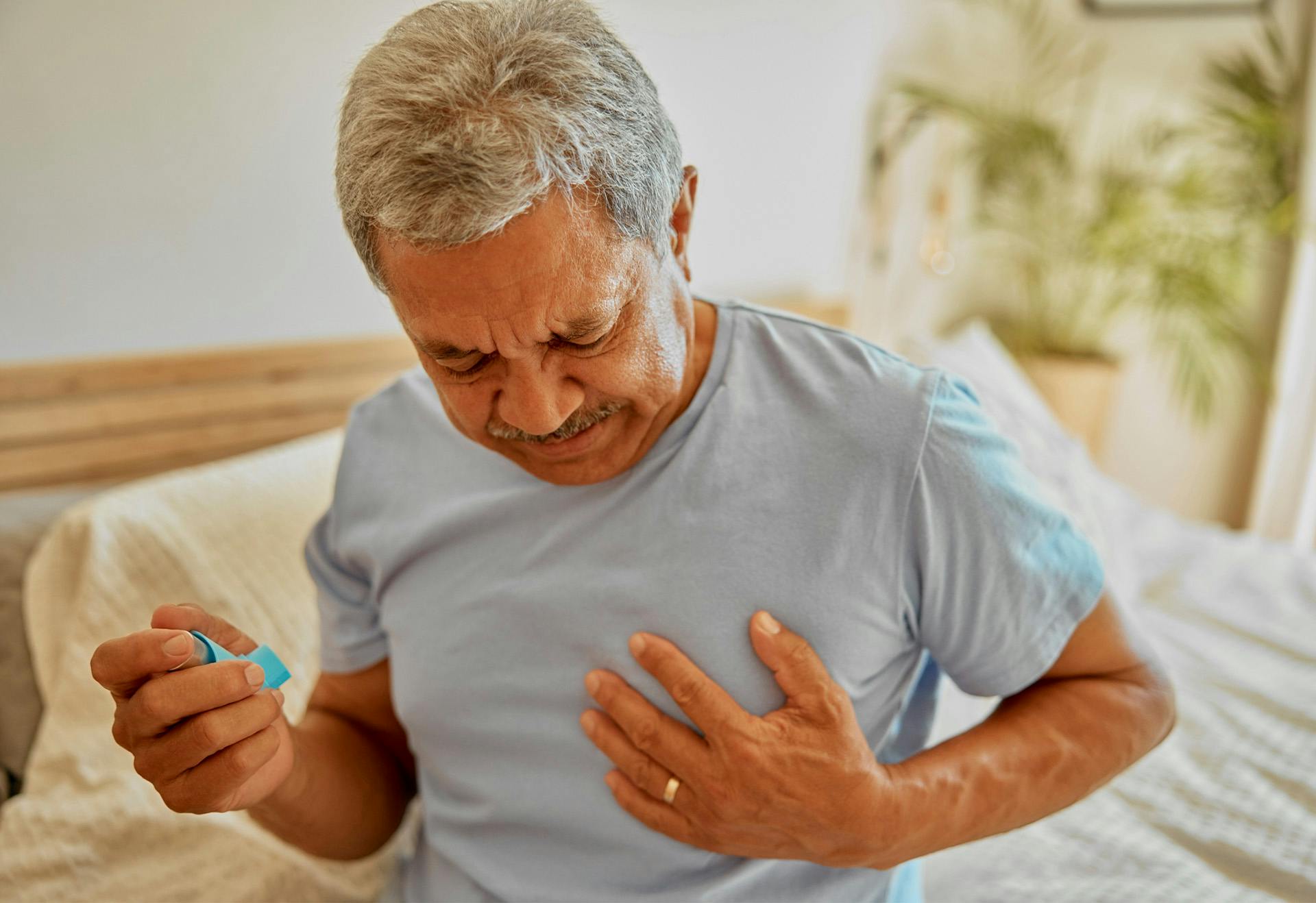 Man sitting in bed in pain holding an inhaler.