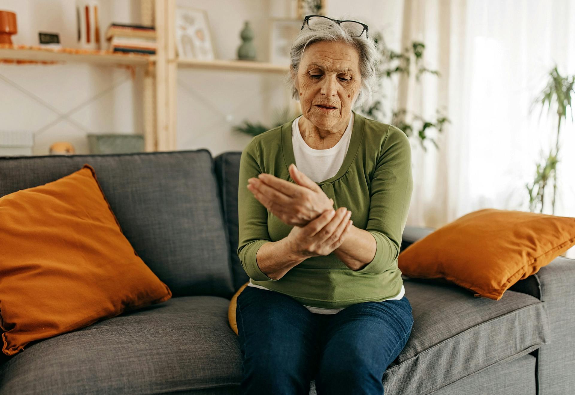 Elderly woman sitting on her couch holding her hand.