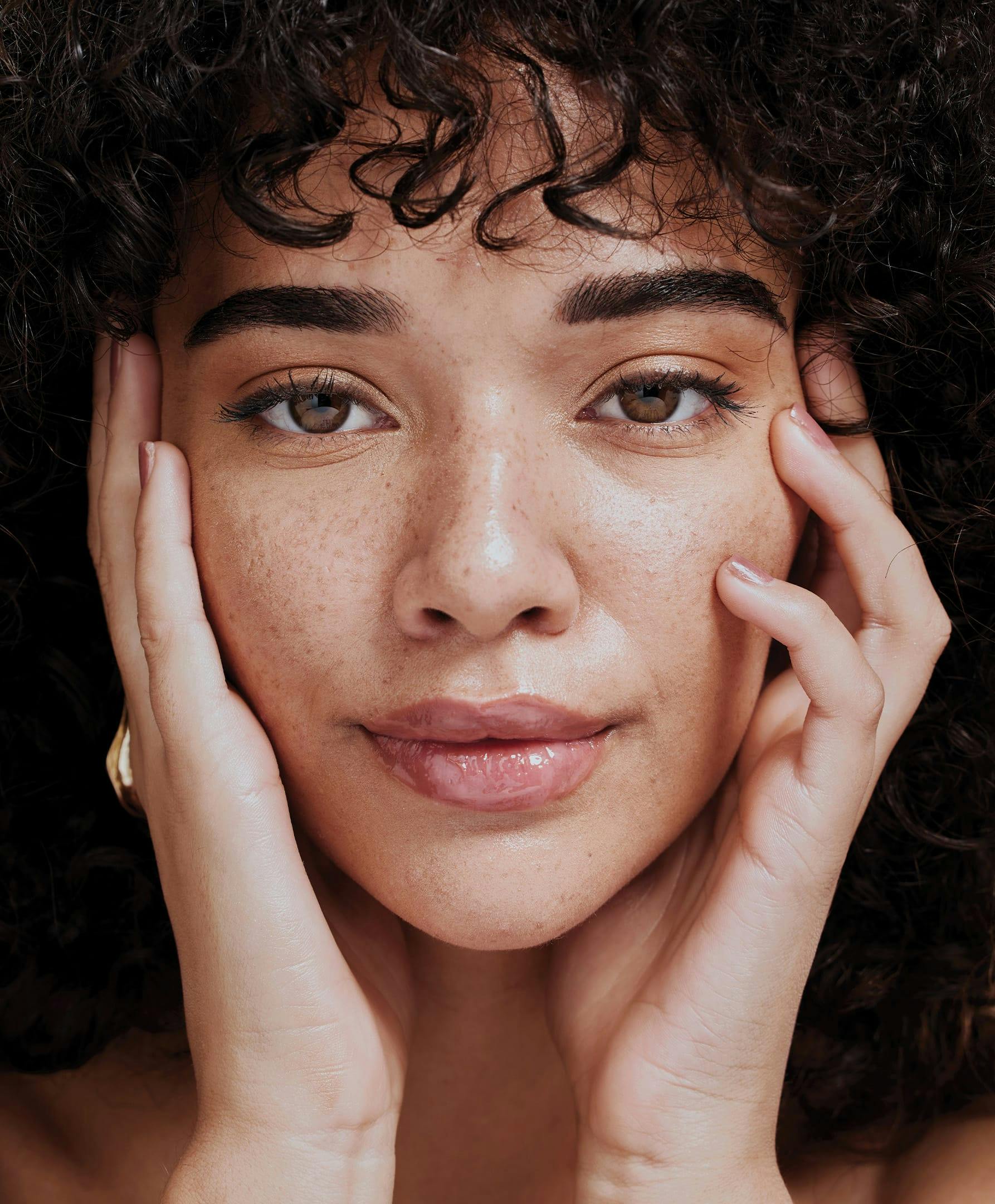 there is a close up of a woman's face with curly hair holding up her hands to her cheeks