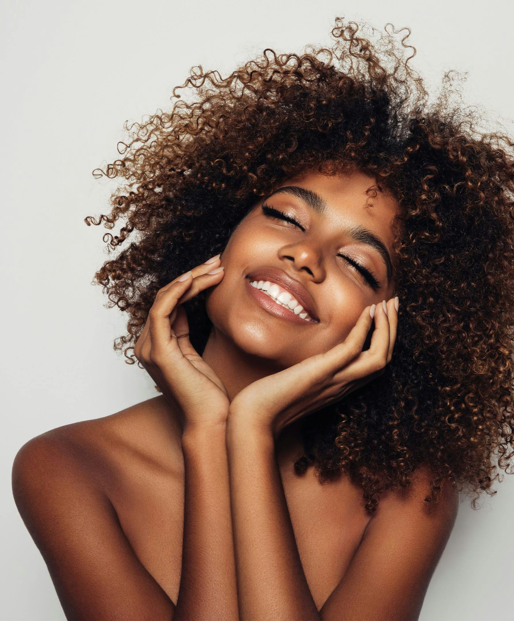there is a smiling woman with curly hair and eyes closed with hands on face