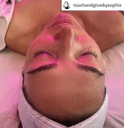 woman with pink light on her face laying on a bed