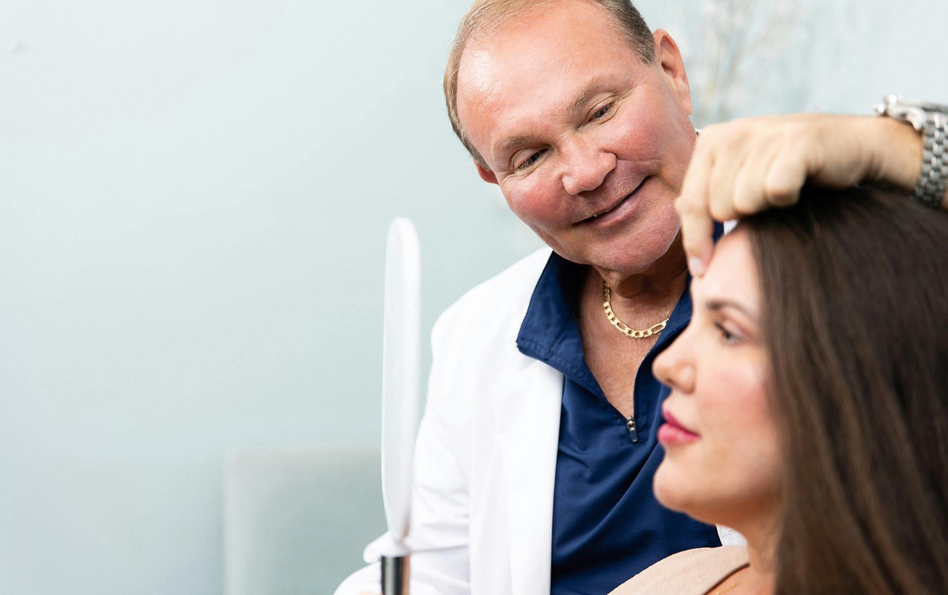 woman holding mirror to her face while doctor points to her forehead