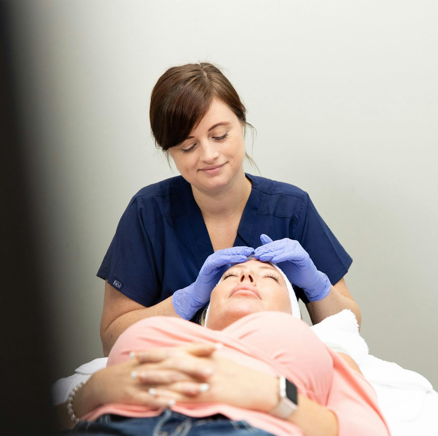 Nurse wearing gloves examines female patient's forehead