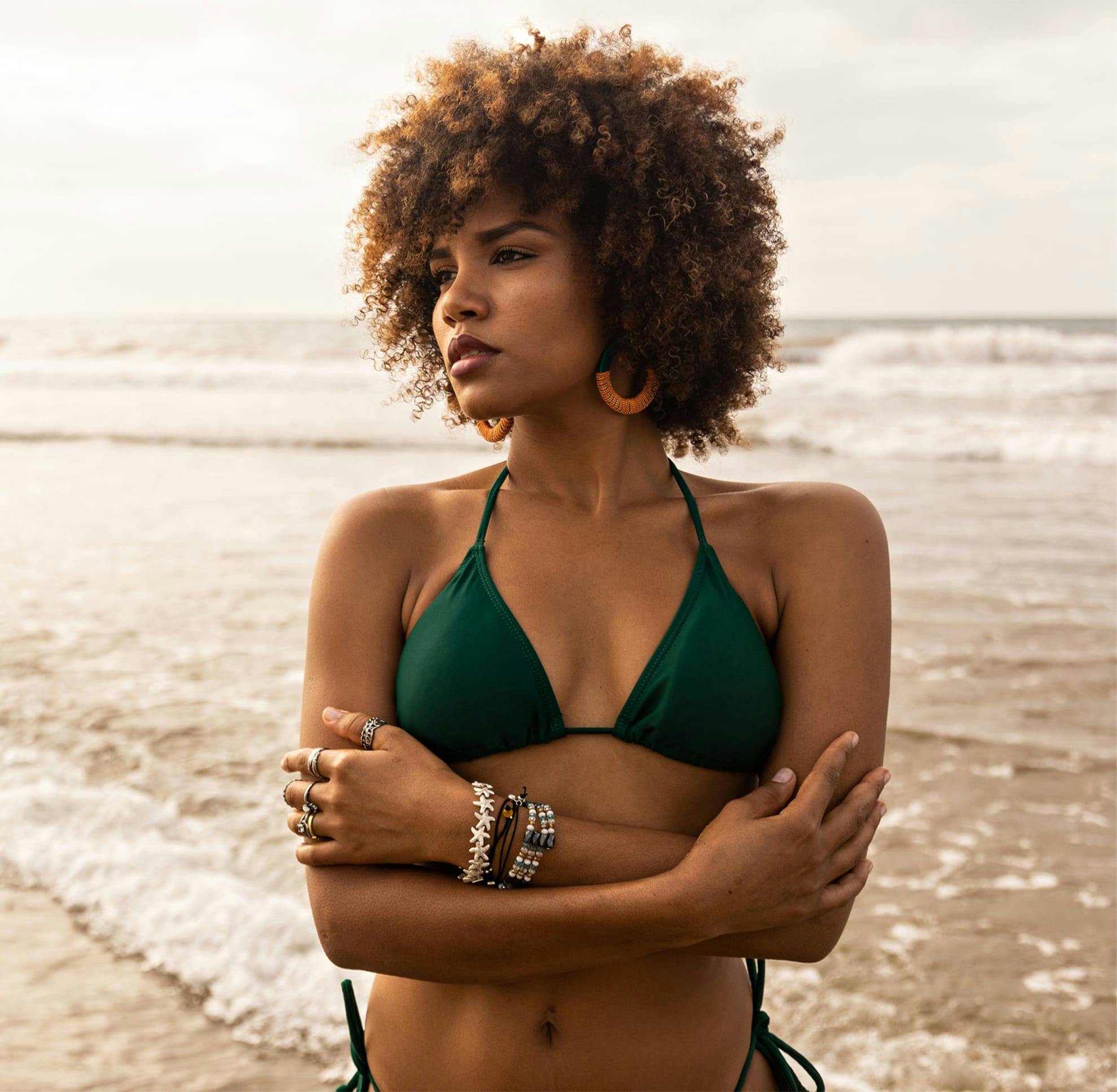 Black woman in a green bikini at the beach with her arms crossed