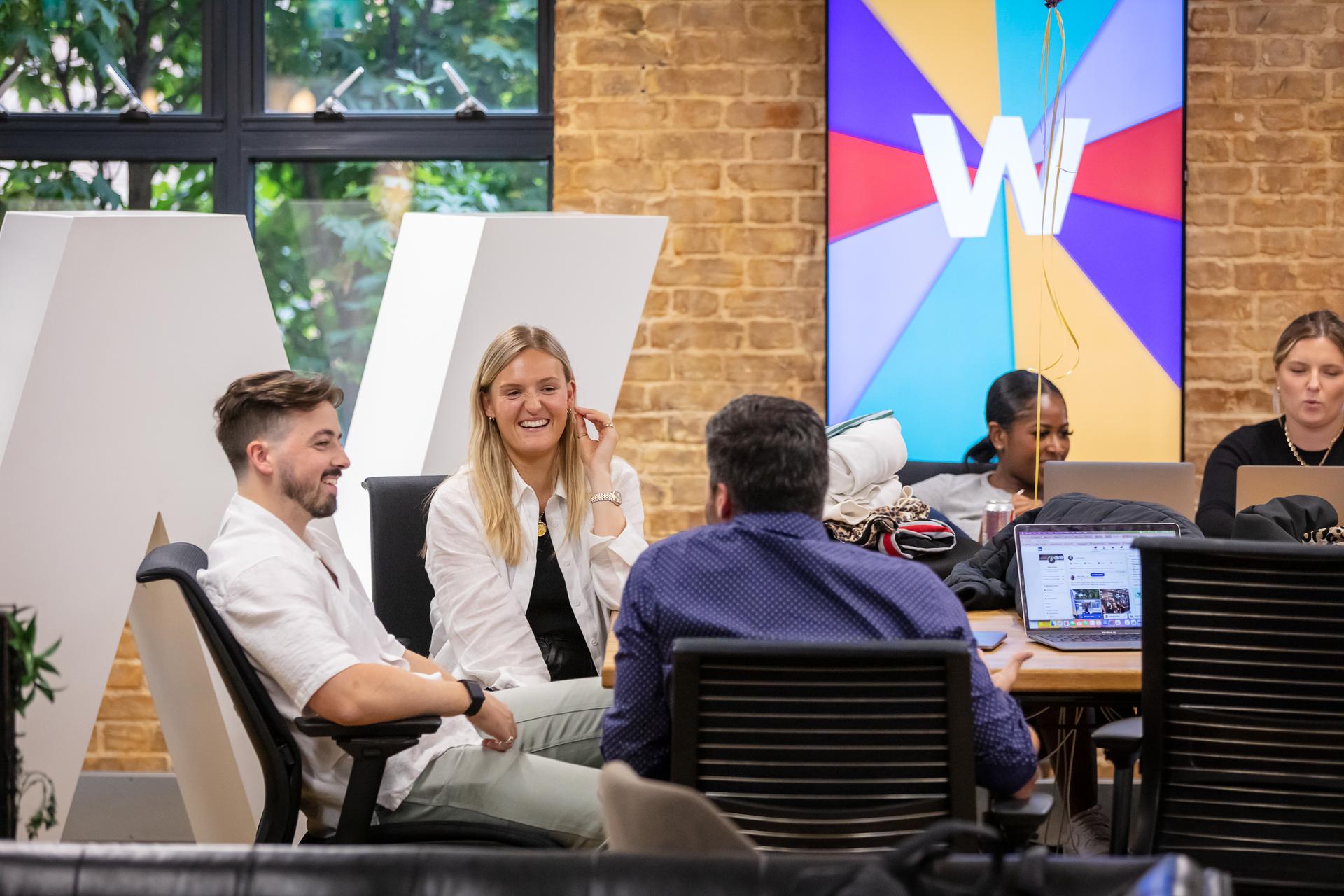 5 colleagues chatting at a busy desk in a bright, colourful office space