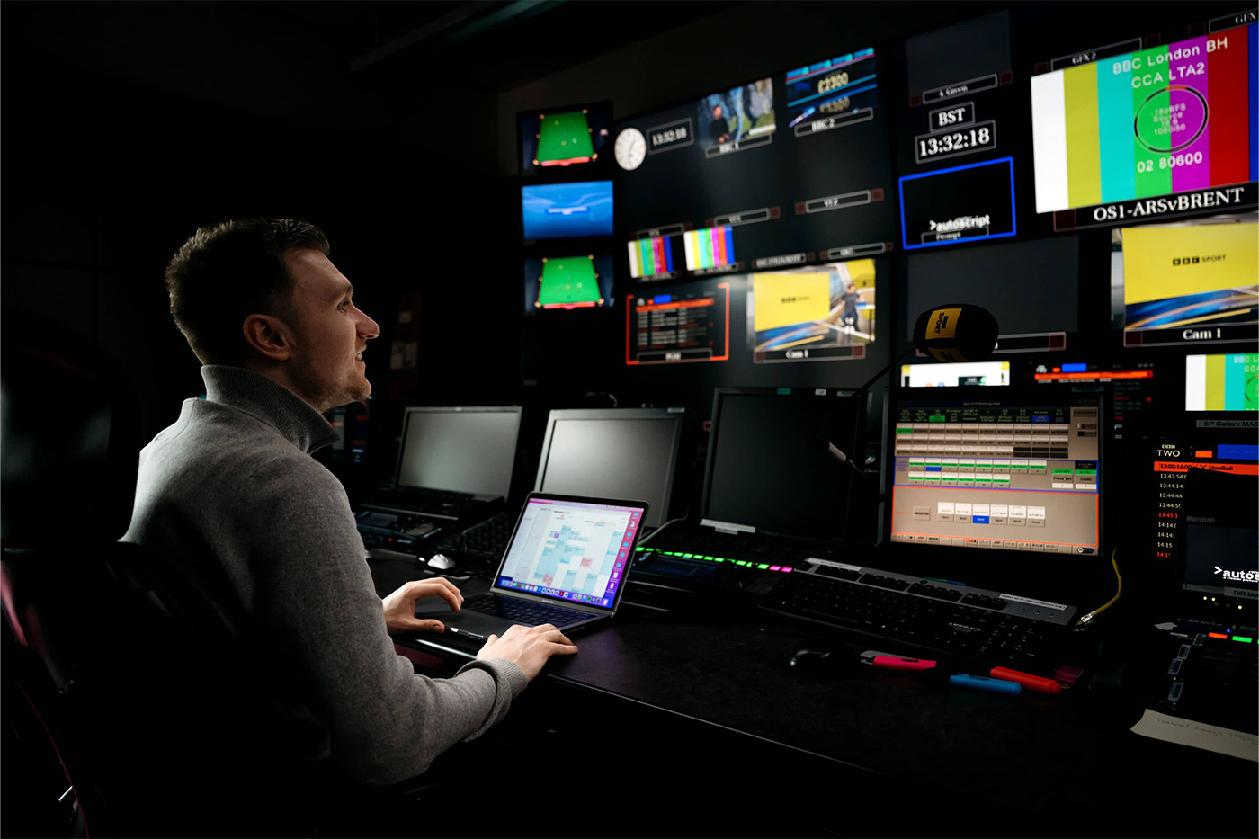 Man in dark production room looking up at multiple screens