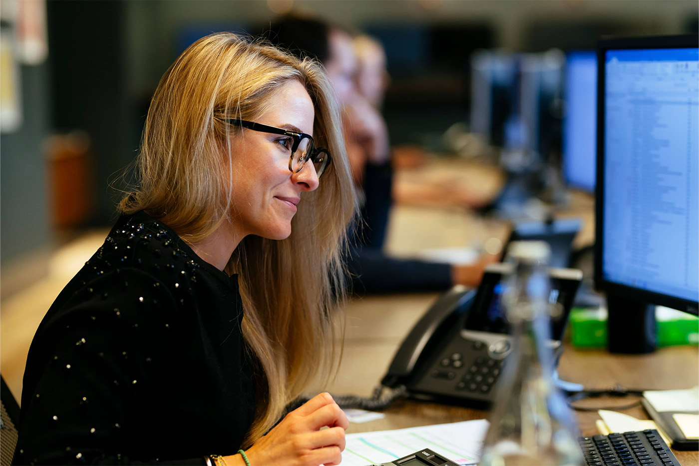 Woman wearing glasses working at a desk with a large screen