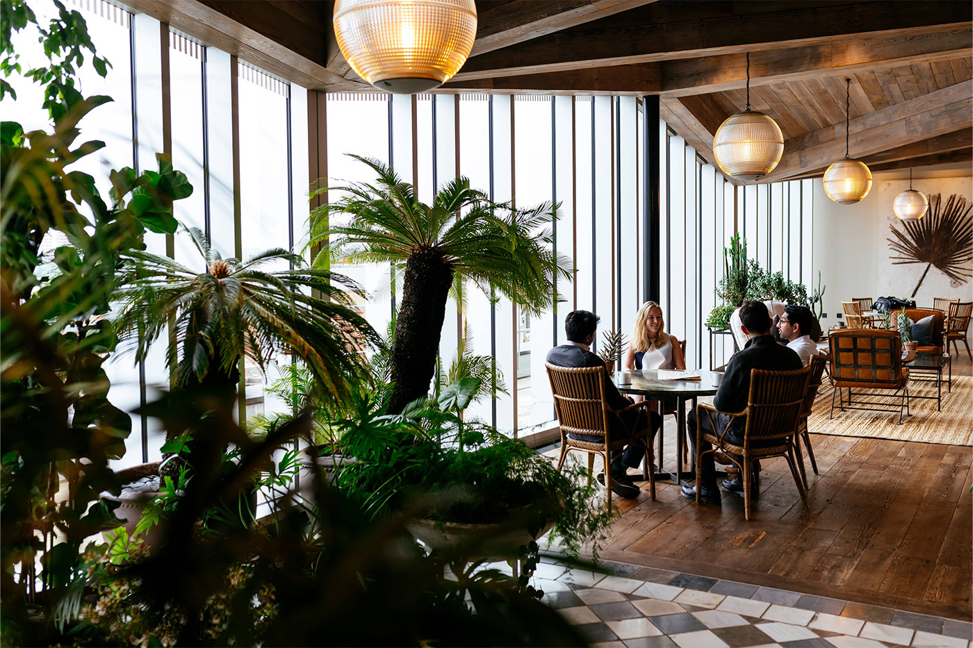 Four colleagues relaxing in a vibrant office space with plants and low hanging lights