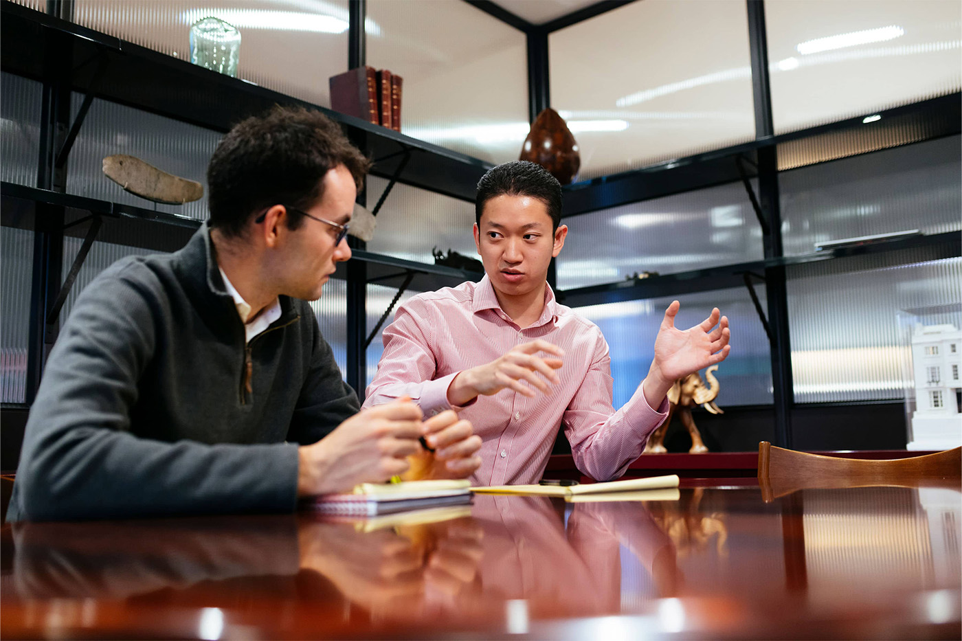 Two men working together over notepads, one man explaining his idea