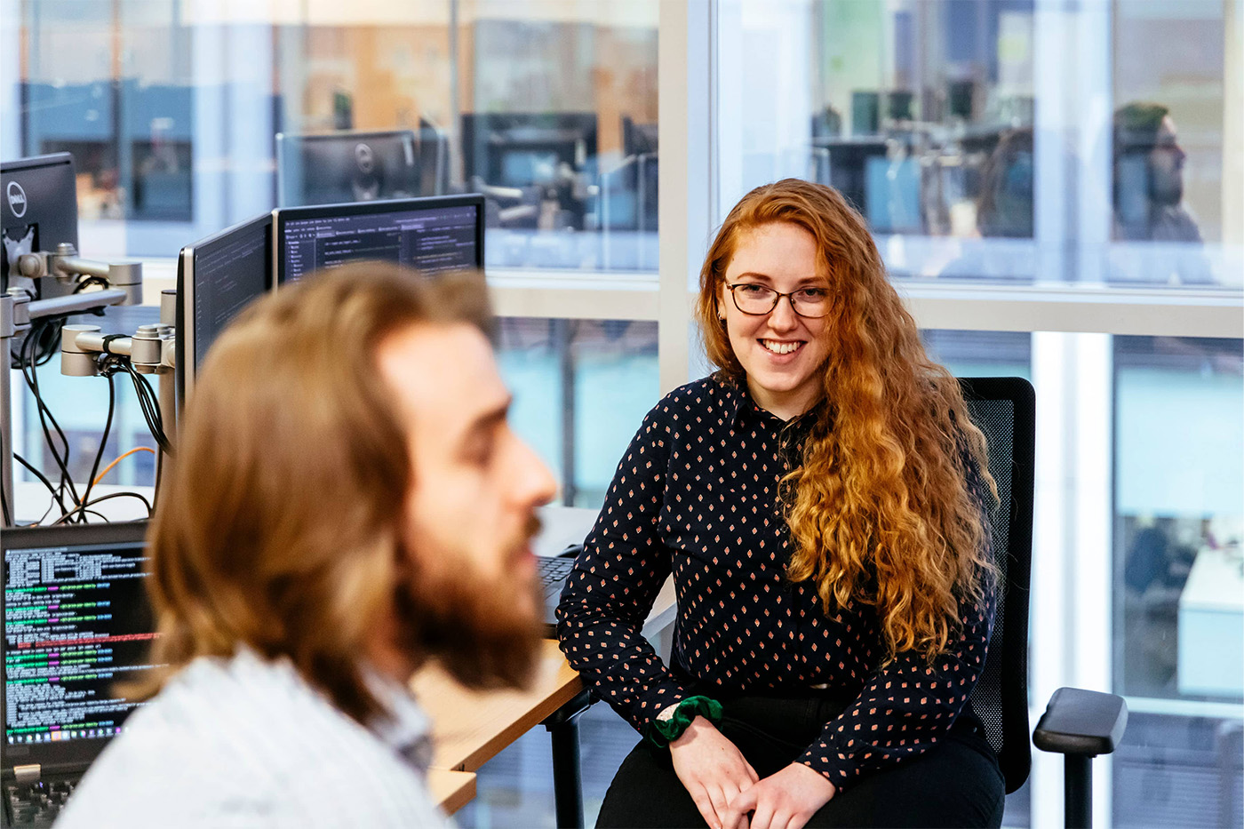 Young woman with long curly hair smiling at male colleague