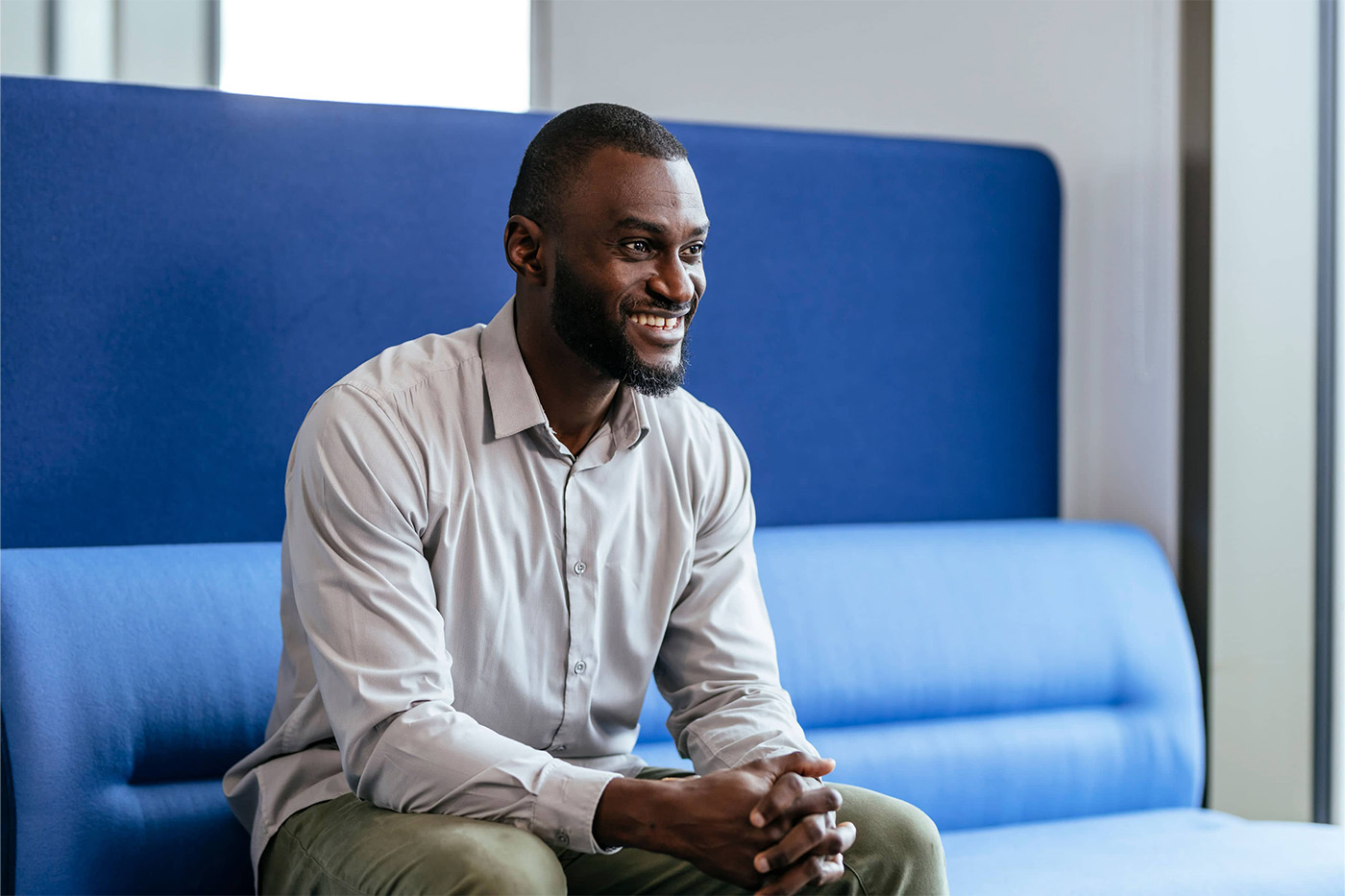 Young man smiling, sat on a large blue bench