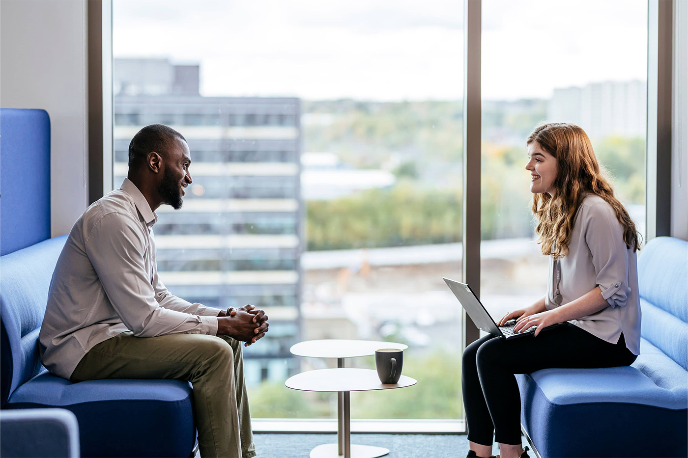 Male and female colleague in an informal meeting space having coffee