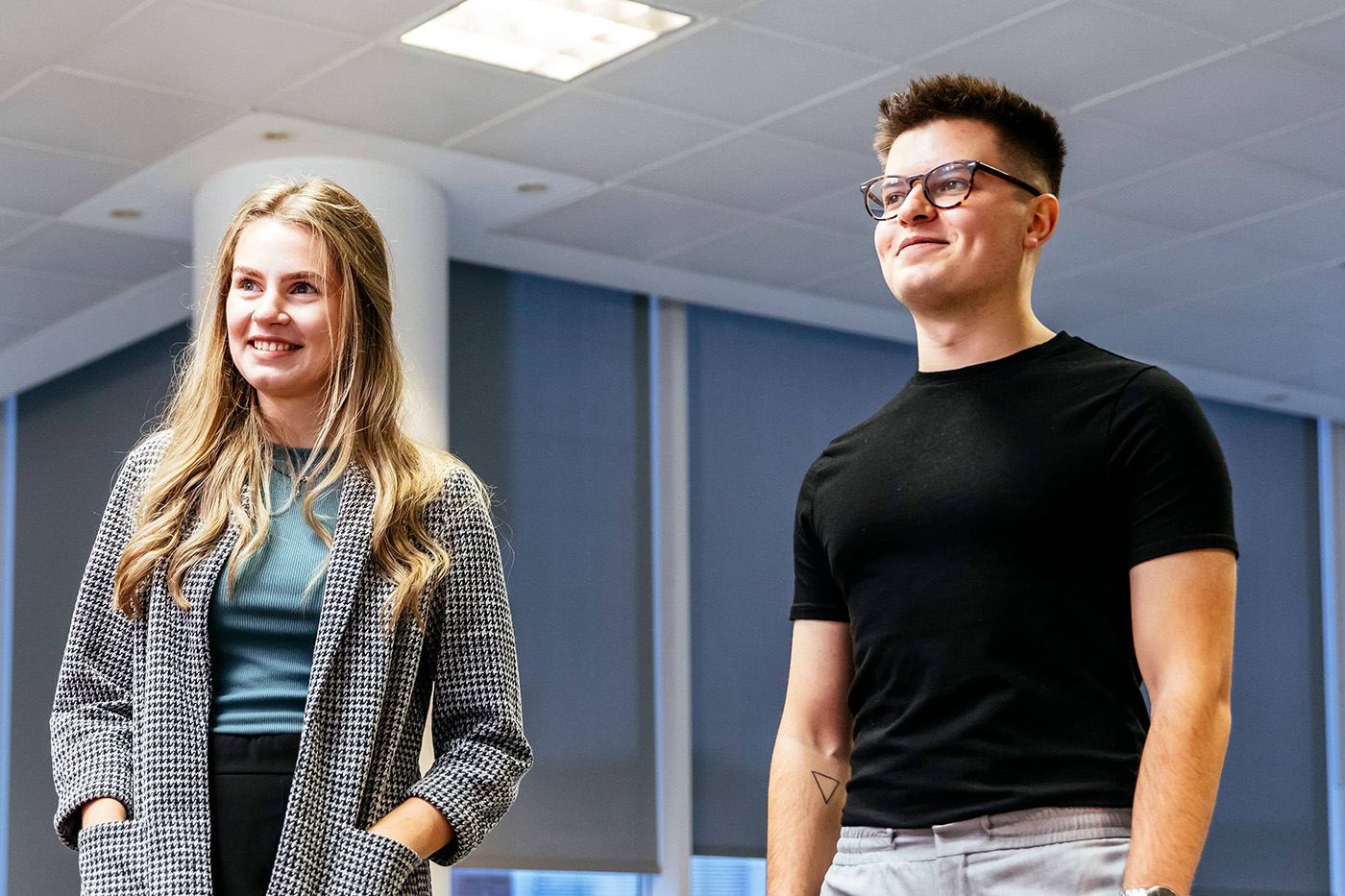 Two colleagues smiling at something in the distance during a standing group meeting