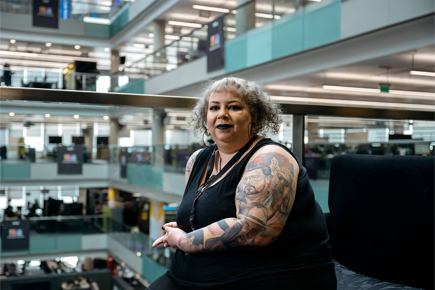 Tattooed woman looking down the camera in a large office