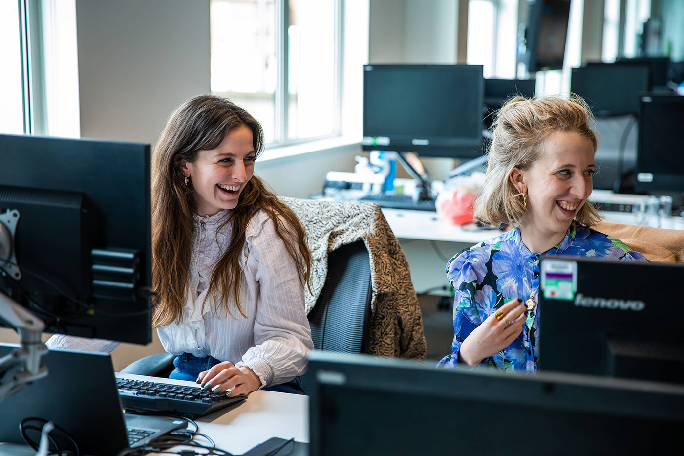 Two women laughing at their desk looking off to the side