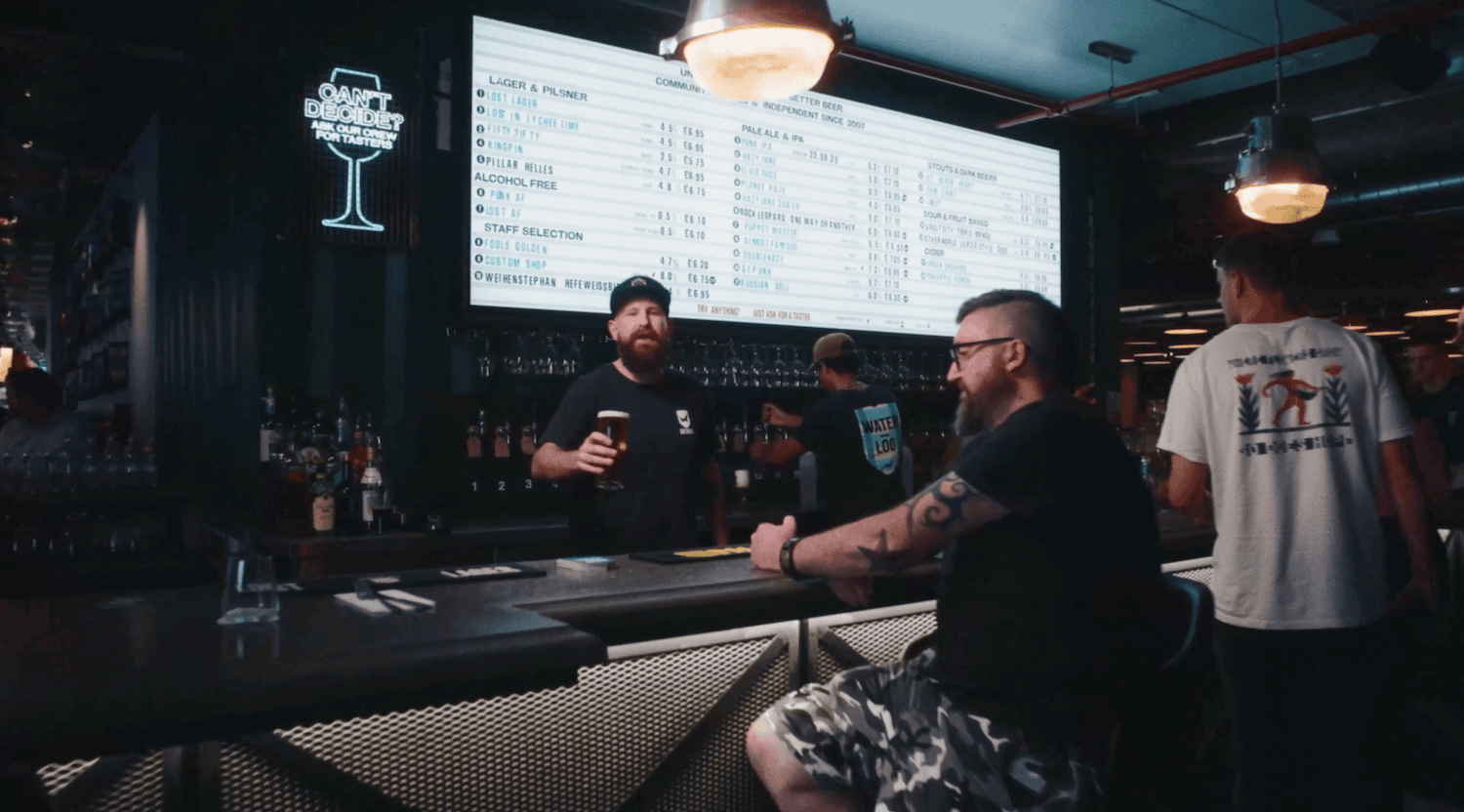 Man behind a bar handing a pint to a customer