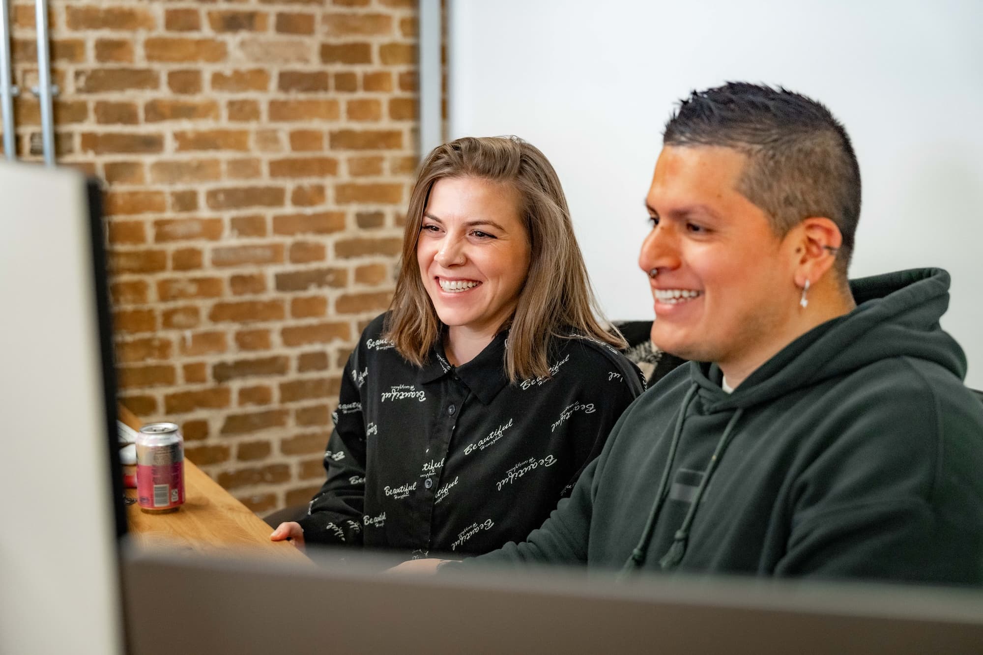 Male and female colleagues smiling happily at desk while working on a big screen together