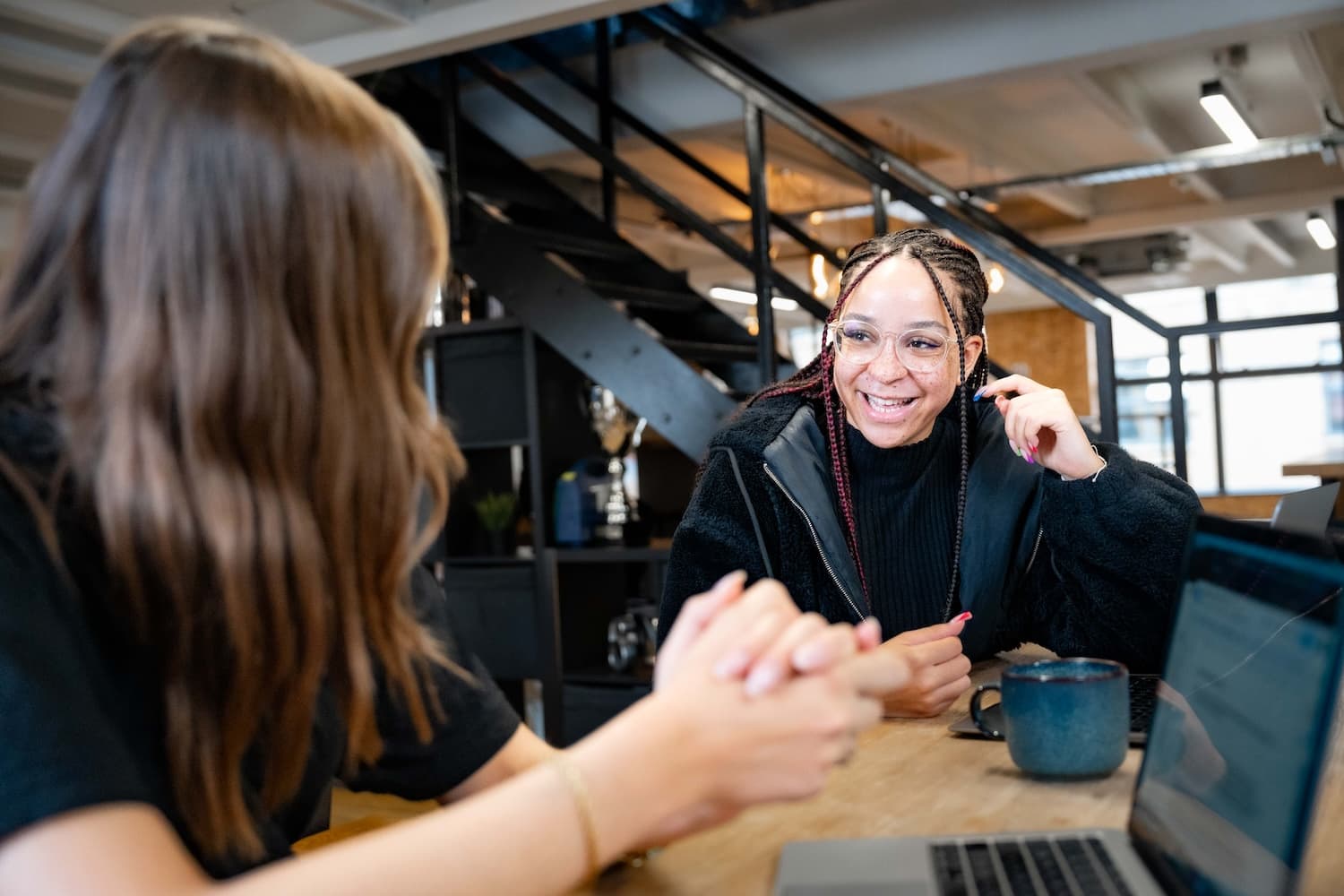Two female colleagues smiling over coffee in an office kitchen