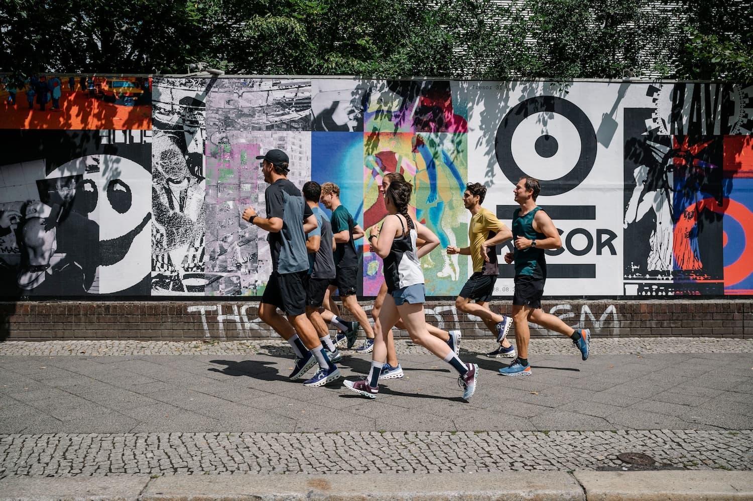 Running group run past a vibrant wall with lots of colourful posters on