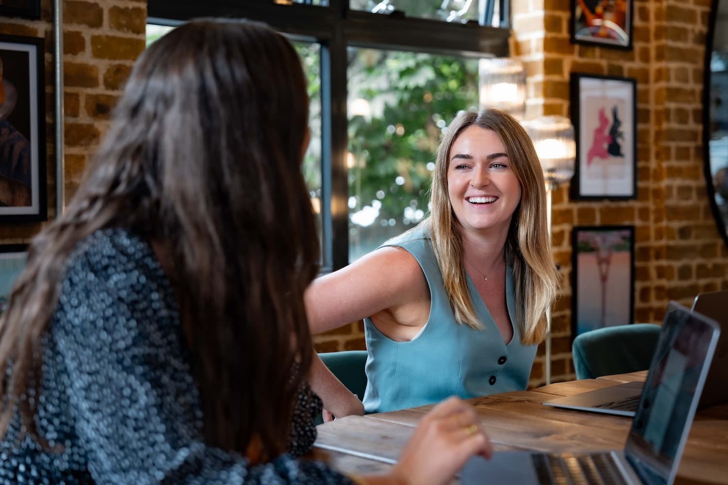 Two female colleagues smiling at each other in bright, artistic meeting room.