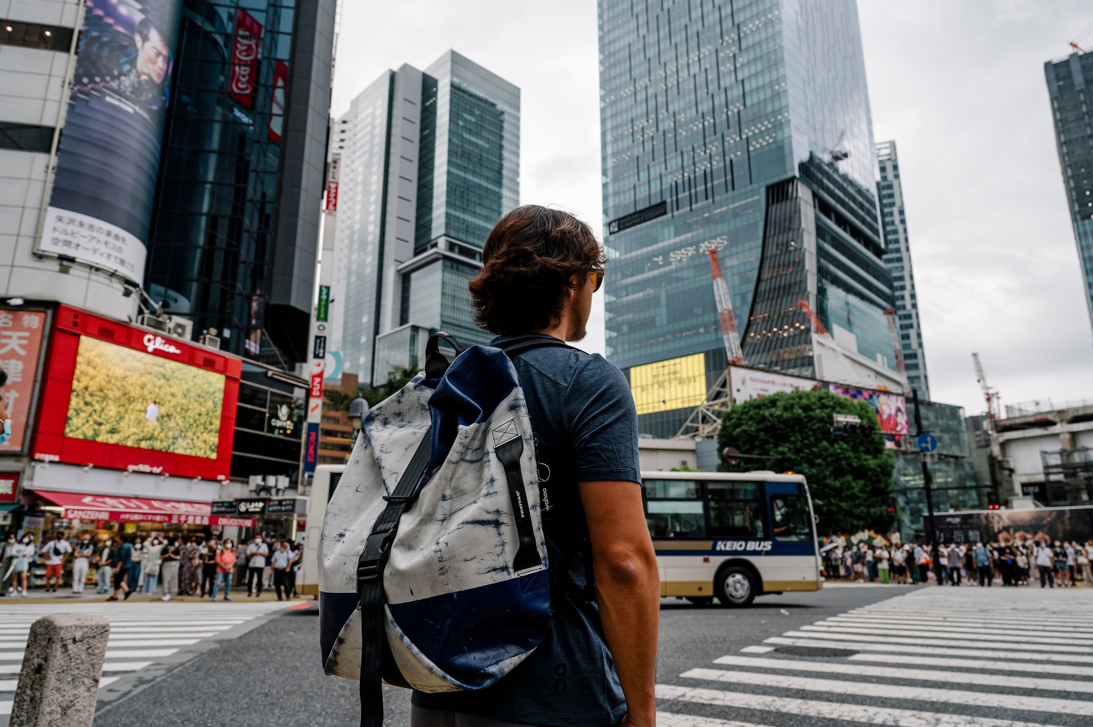 Man wearing backpack looking out into a busy crosswalk