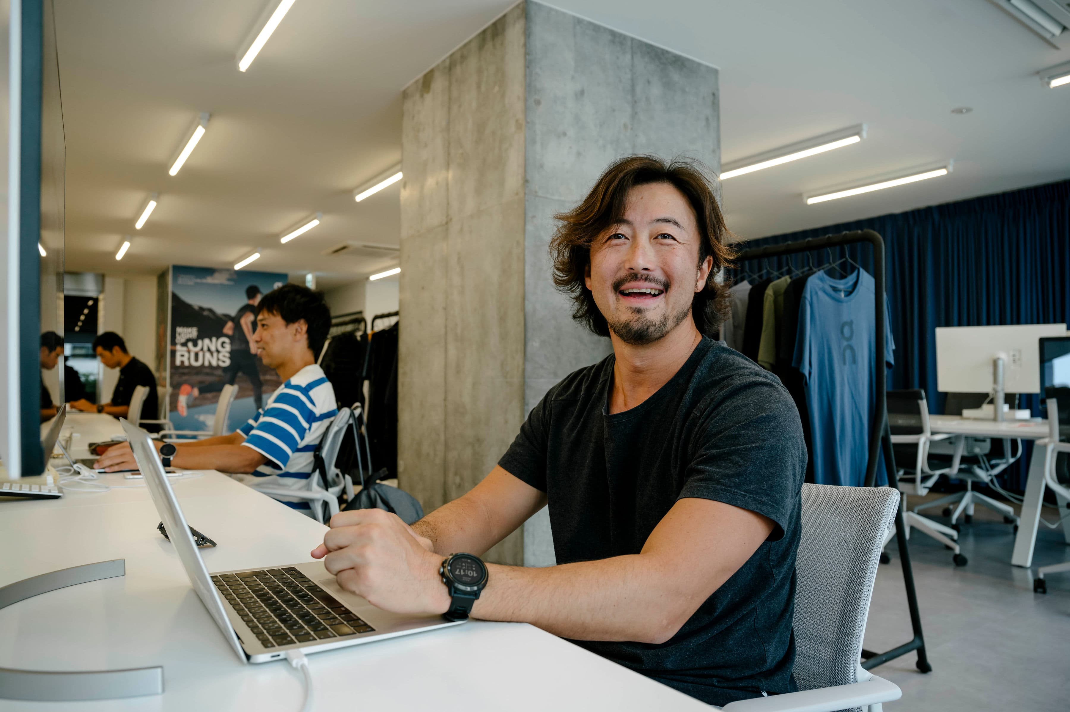 A man in a busy office smiles at the camera