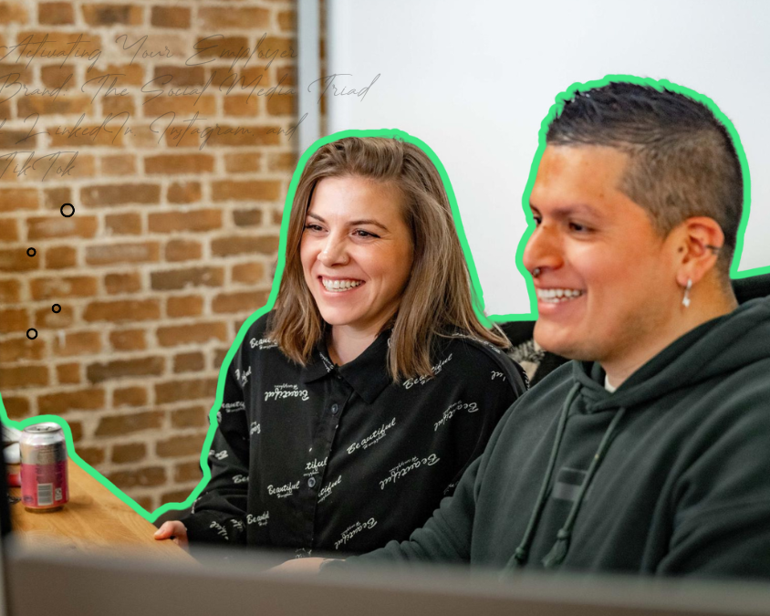 Male and female colleagues smiling happily at desk while working on a big screen together