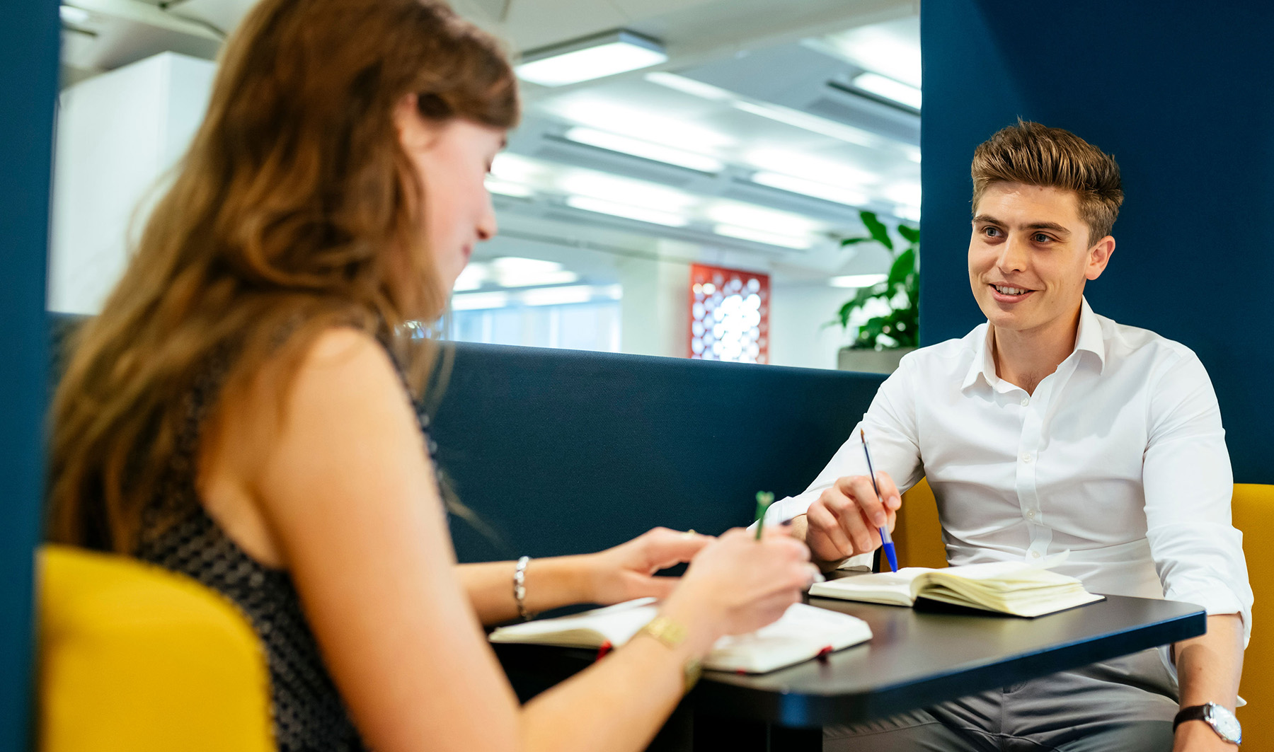 Male and female colleague having a one to one meeting using notepads