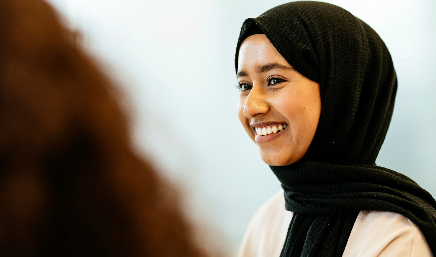 Young female Knight Frank employee wearing a head scarf smiling during a meeting
