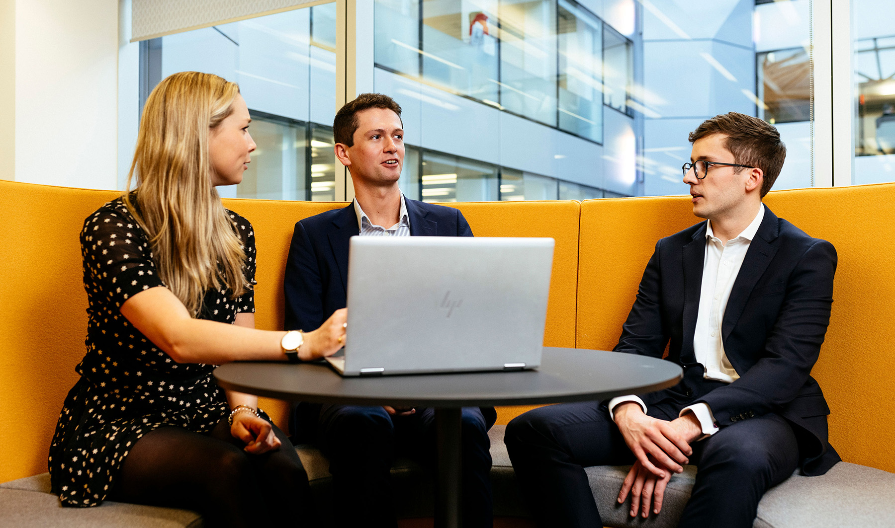 Group of three colleagues having a meeting together working on one laptop in a bright, colourful office