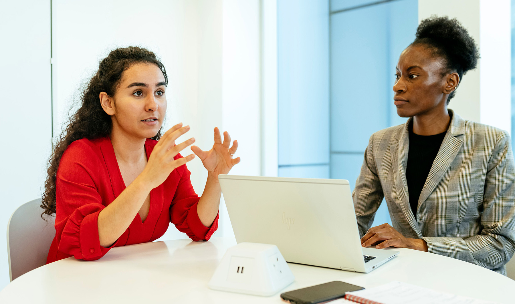 Two women dressed formally discussing ideas over a laptop