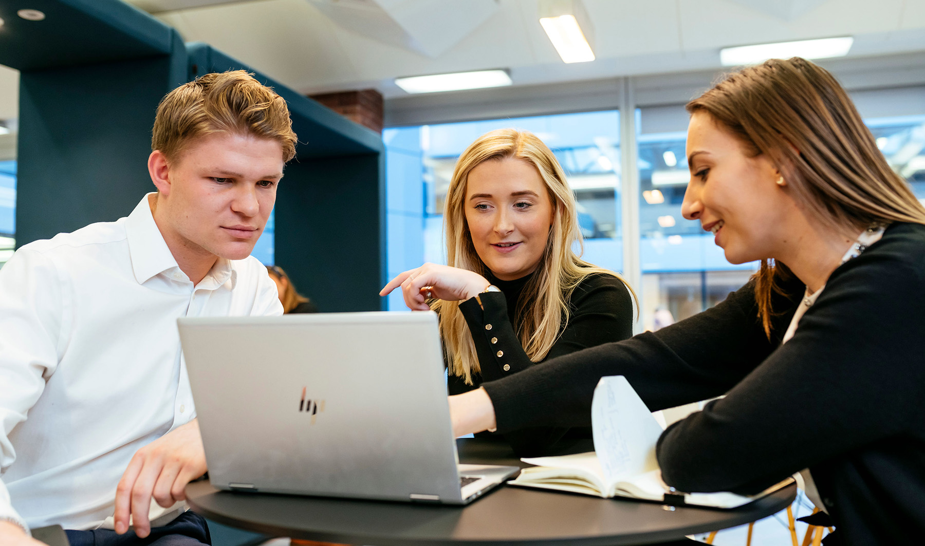 Three young adult colleagues in a meeting working over a laptop in a bright office with dark green walls