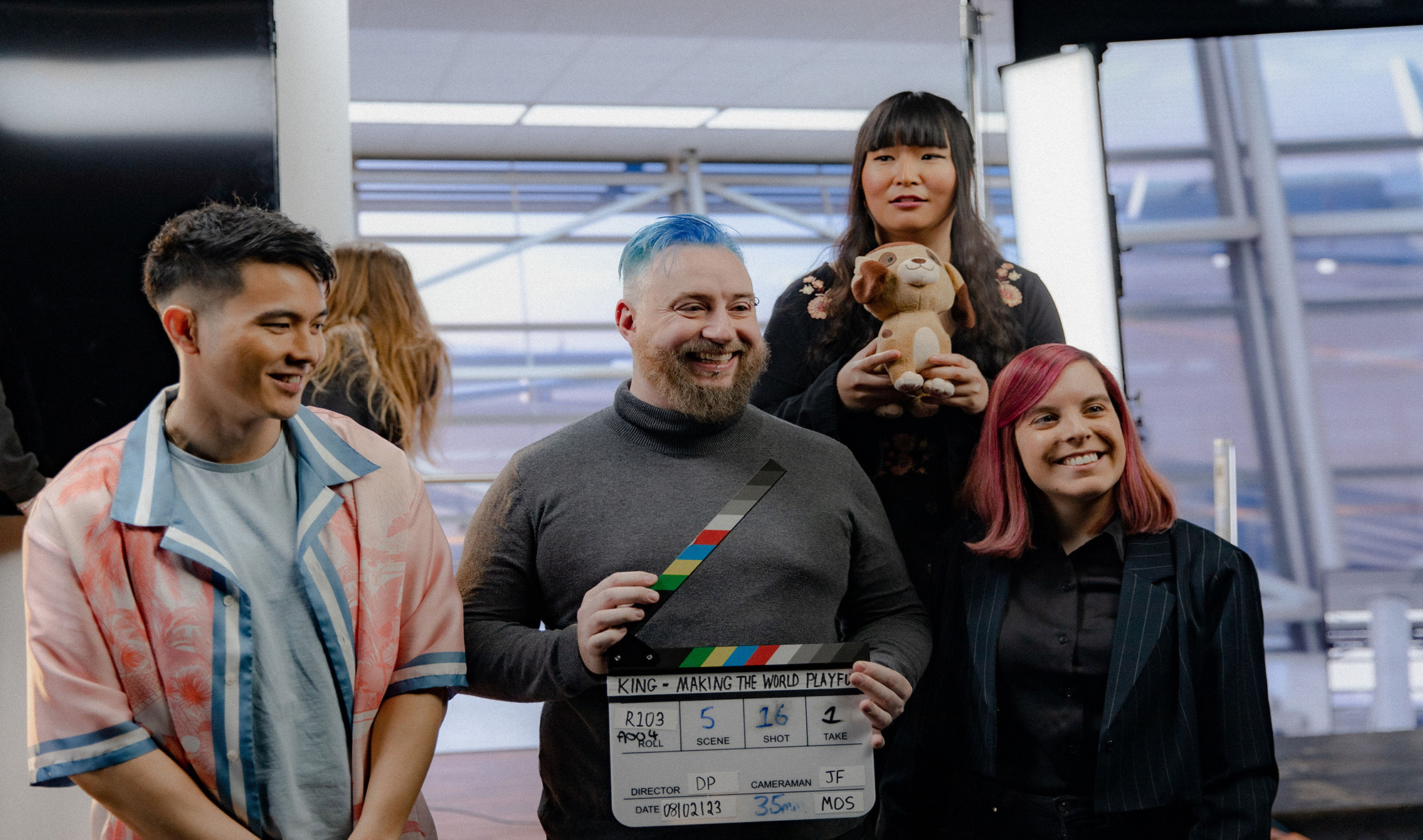 Behind the scenes shot of a group of actors on set holding a clapper