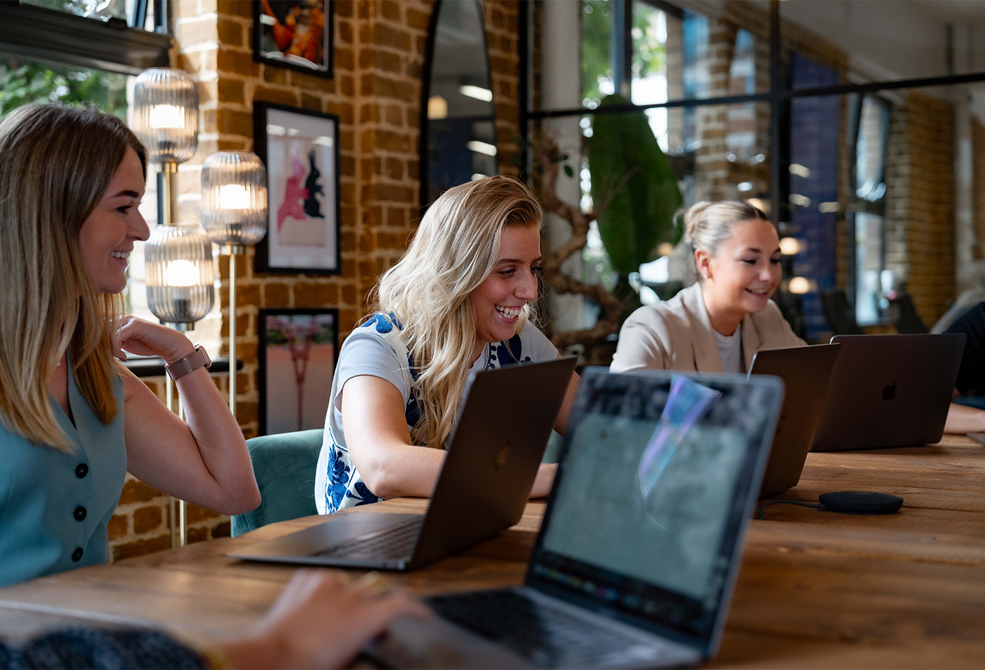 Image of three woman on laptops, smiling during a business meeting