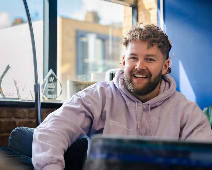 Photo a male in a purple jumper with a window behind him smiling