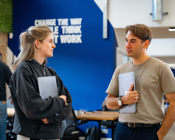 Photo of male with brown hair talking to female with blonde hair in an office standing up