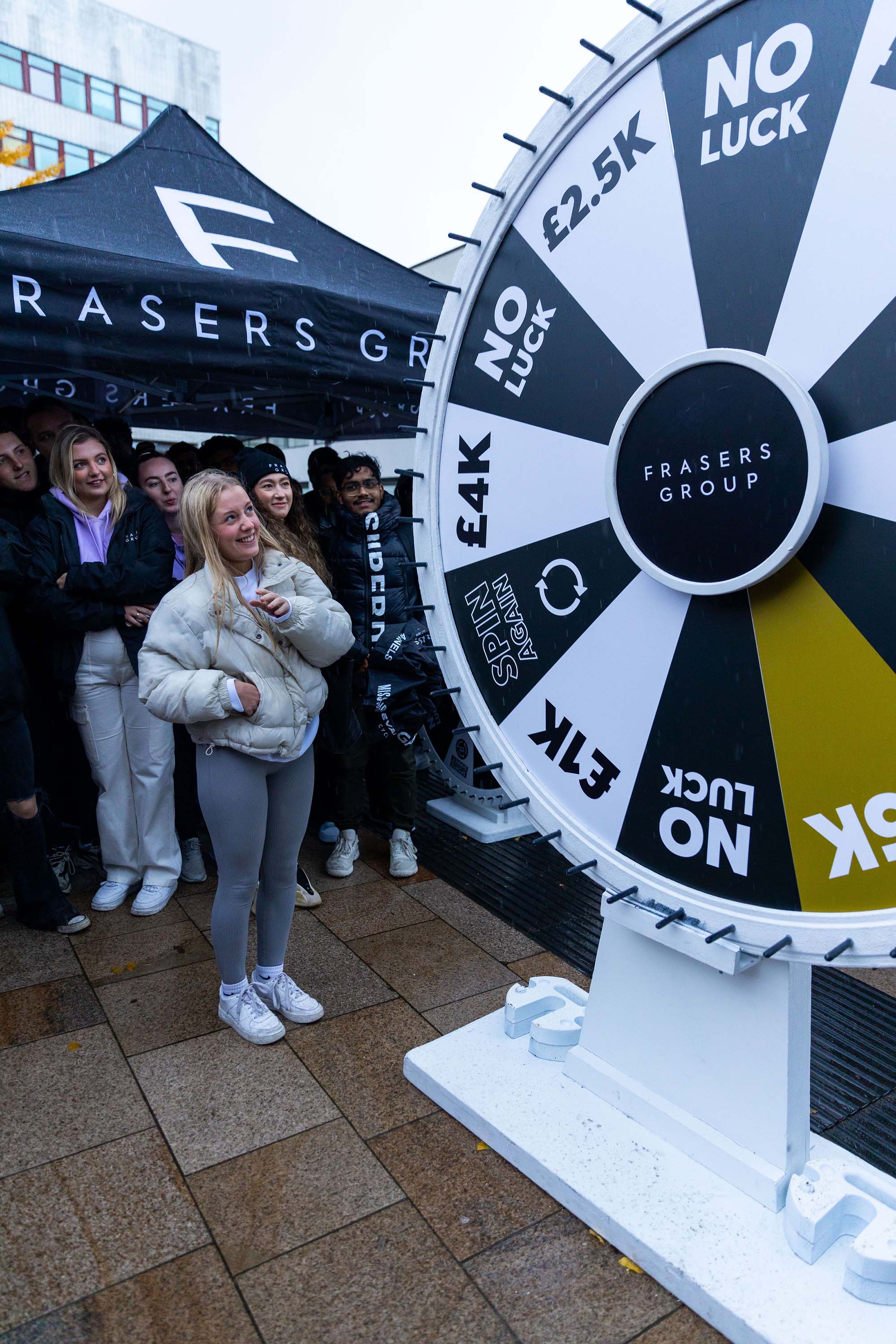 Image of young blonde woman spinning a huge wheel in Frasers Group branding