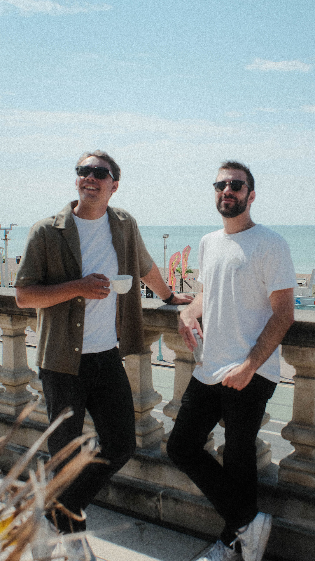 two friends smiling with coffee by the sea