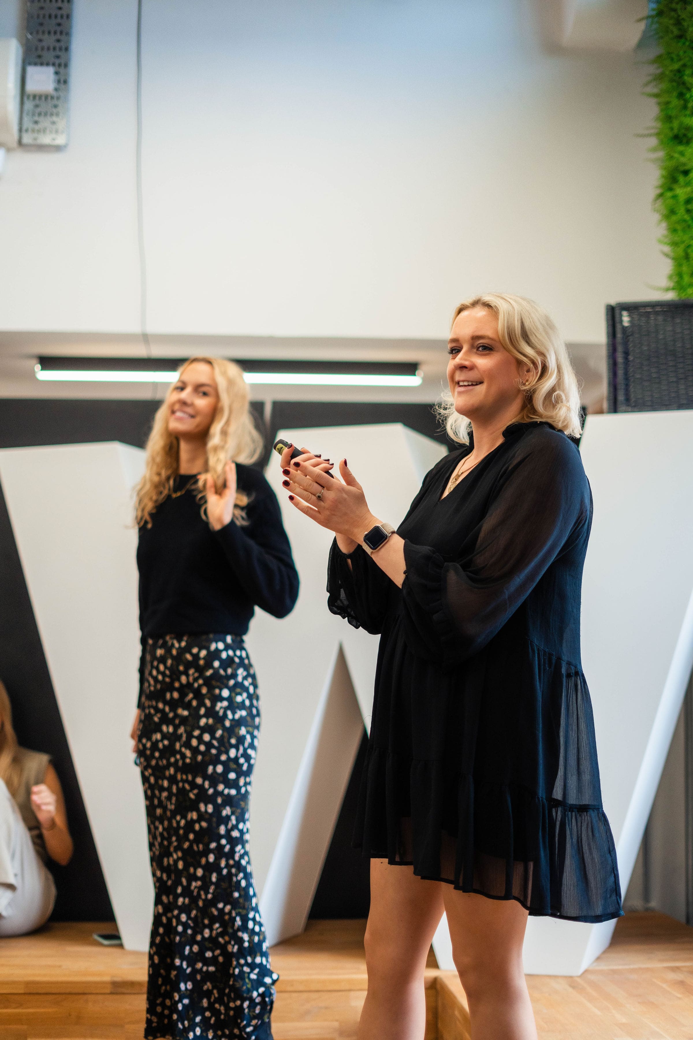Two blonde females give a presentation in front of a large white W