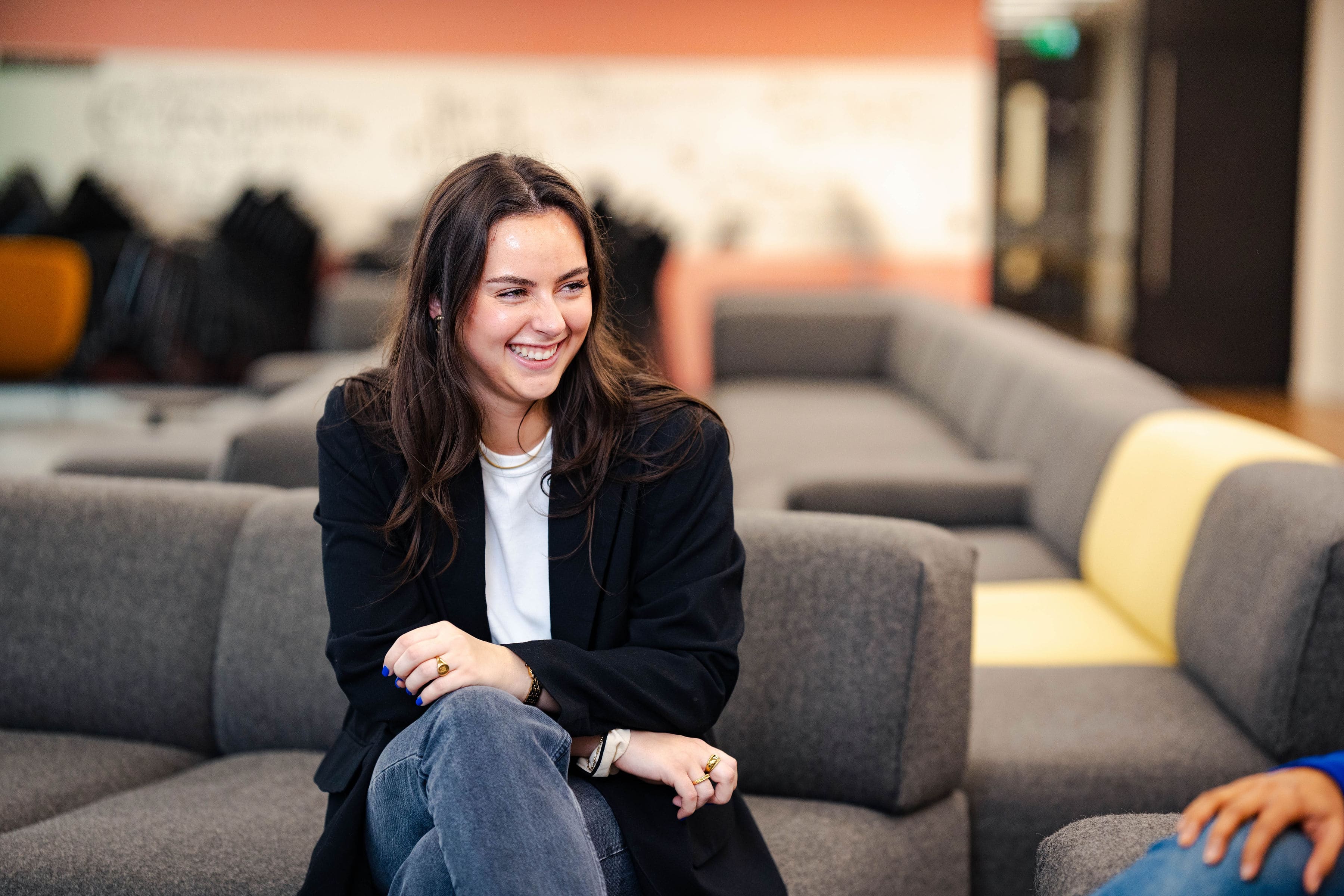 White brunette woman with white t-shirt and black blazer smiling in the Trainline office
