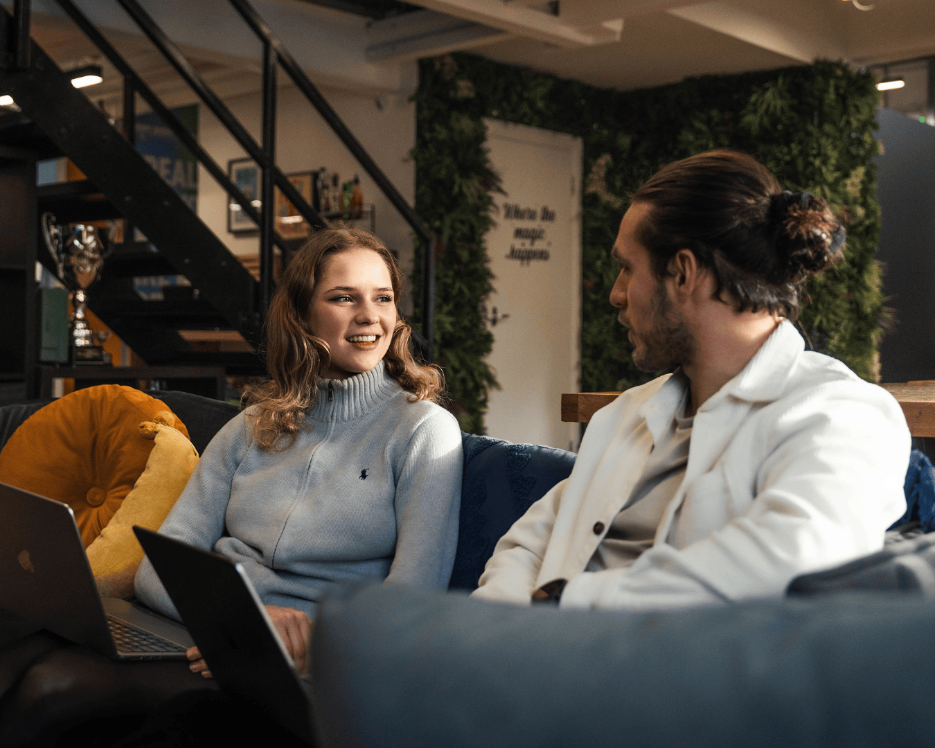 photo of two people sat on sofa with laptops having a meeting